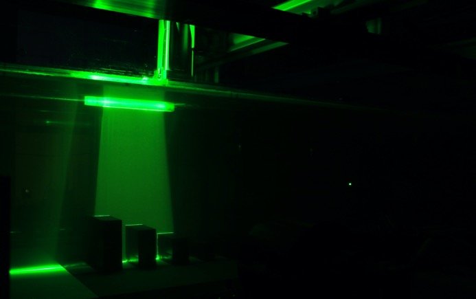 A green laser sheet illuminating model buildings in the dark fluid tunnel
